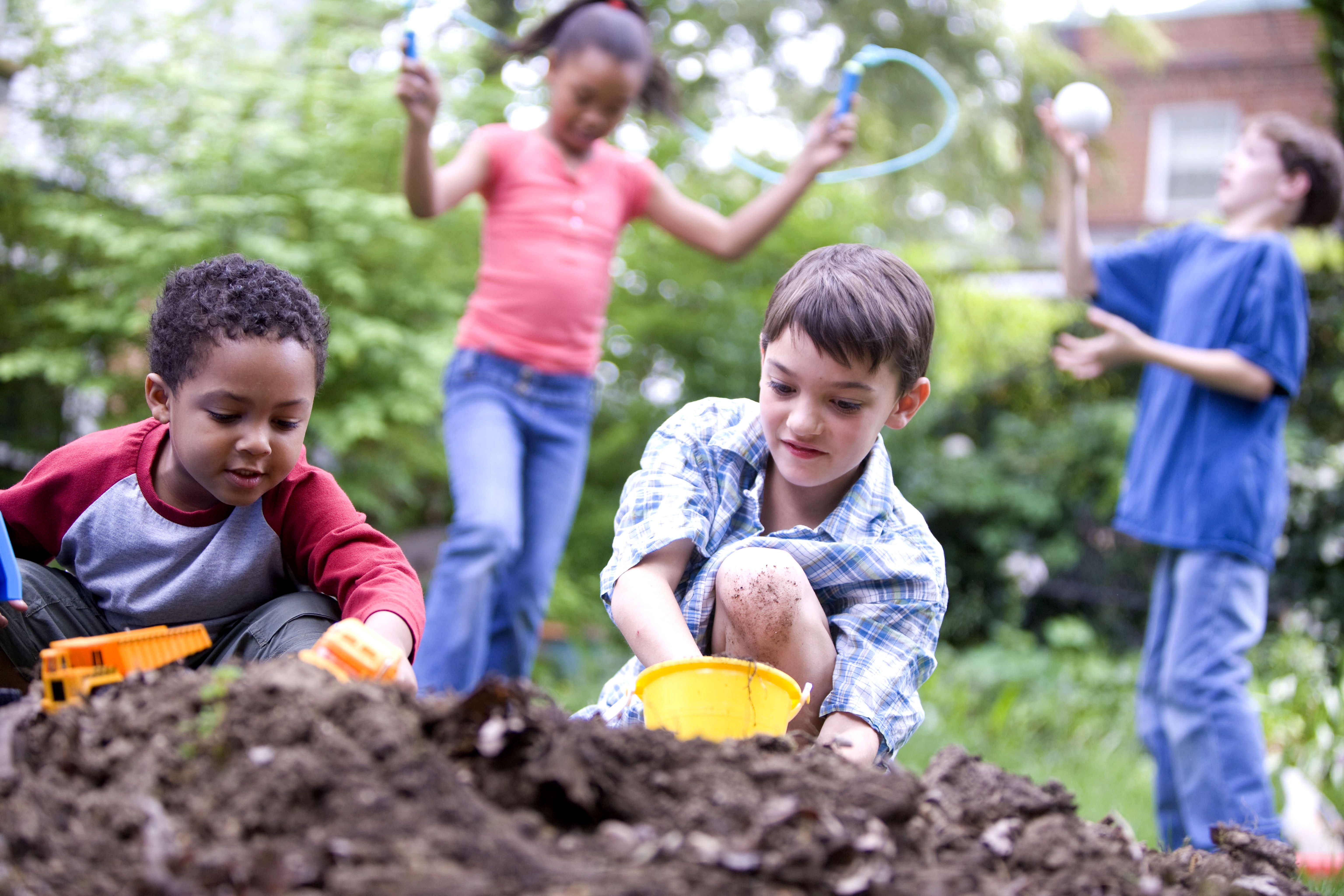 Children sharing outdoor play with toy trucks, a skipping rope, and a ball.