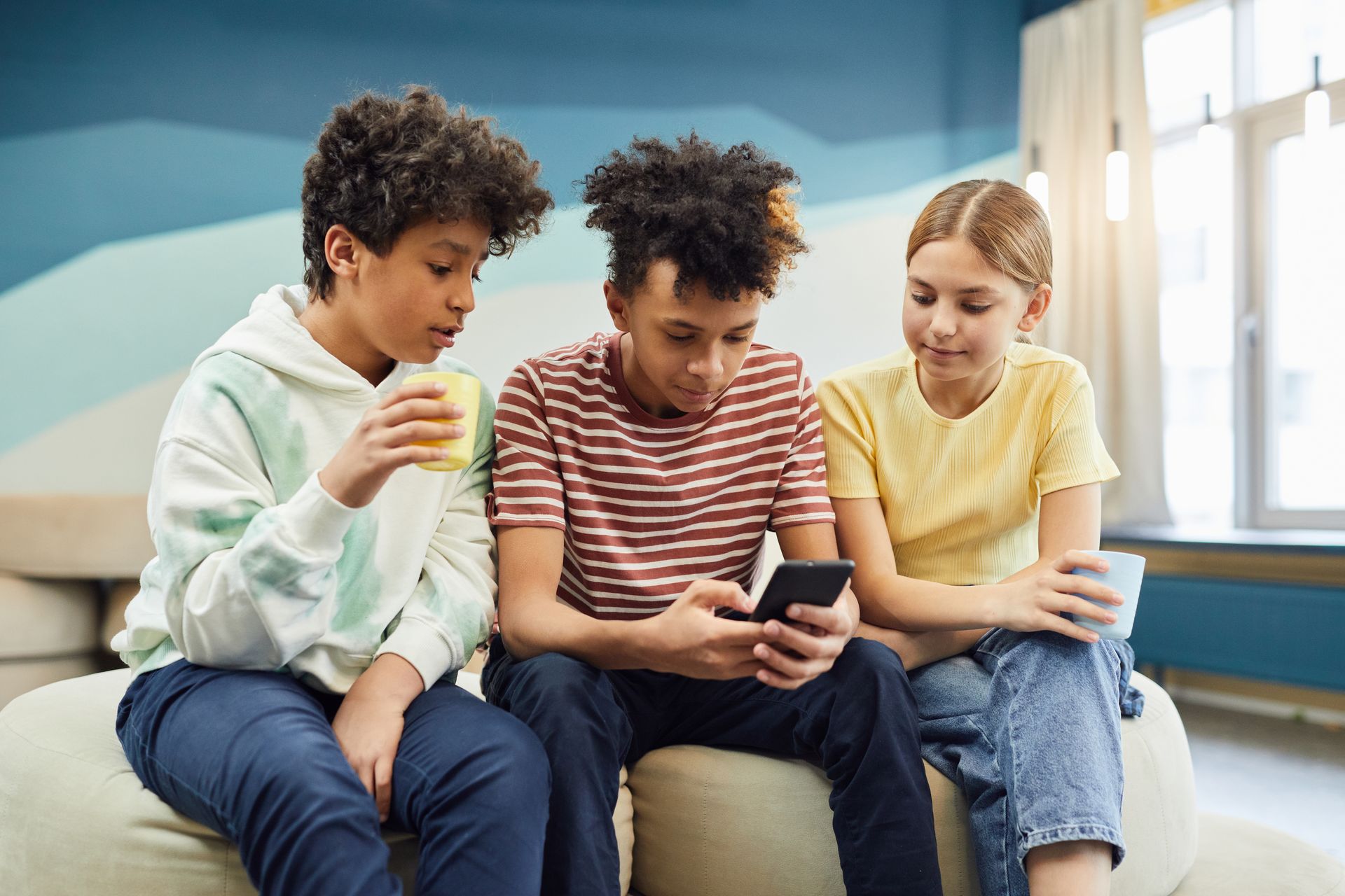 Three teenagers sitting together and looking at a smartphone.
